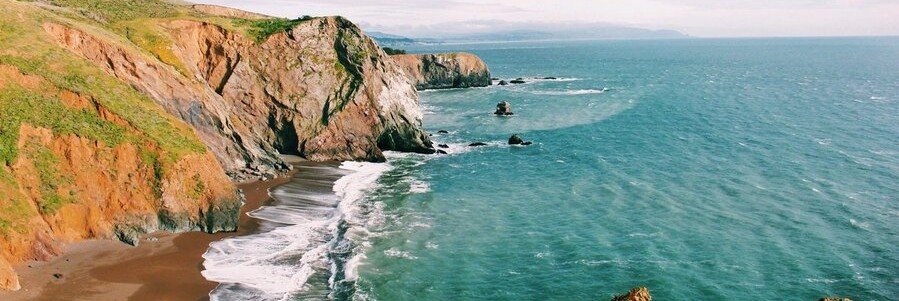 Rugged Marin County coastline with steep cliffs, turquoise water, and a quiet black sand beach along the Northern California coast