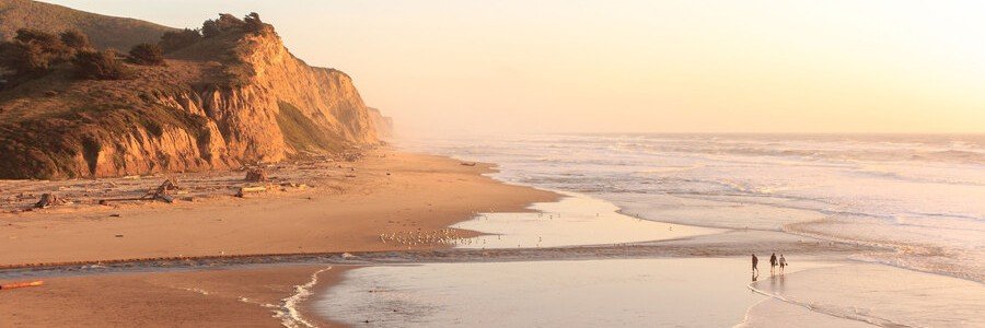 Golden sunset over San Gregorio State Beach in San Mateo County, California, with coastal cliffs, gentle waves, and a wide sandy shoreline