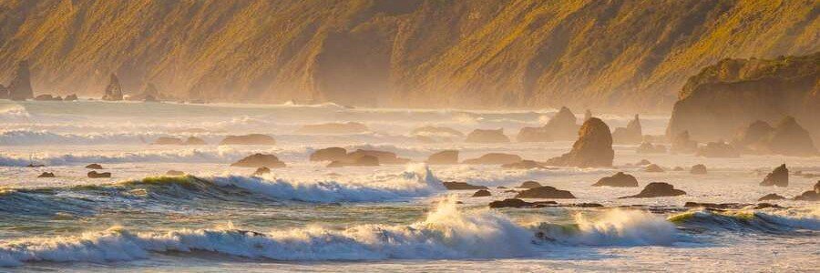 Golden sunset over Sea Glass Beach in Mendocino County, California, with foamy waves, rocky shoreline, and steep coastal cliffs
