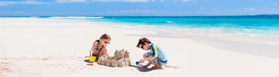 Children building a sandcastle on a sunny beach with turquoise water in the background.