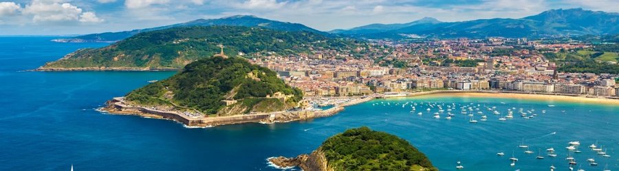 Panoramic view of San Sebastián’s La Concha Bay with turquoise water, green hills, and a bustling seaside city.