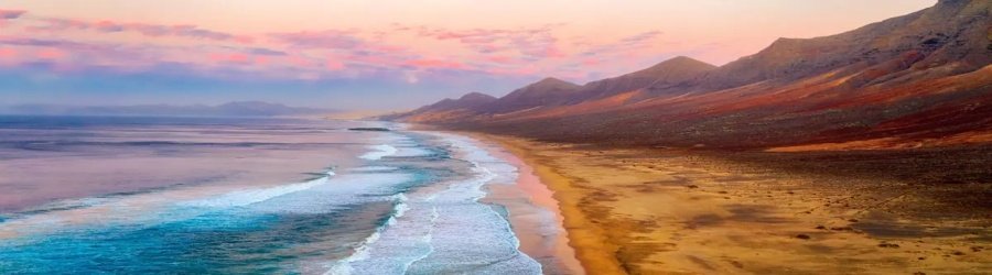 Expansive beach and rolling waves stretch along Fuerteventura’s wild coastline at sunset.