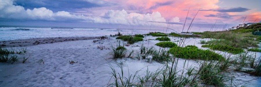 Soft pastel sunset colors over the sandy shoreline and dunes of Cocoa Beach, Florida.