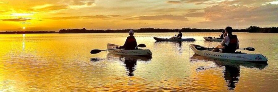 Kayakers paddling across calm waters during a colorful sunset on Florida's Space Coast.