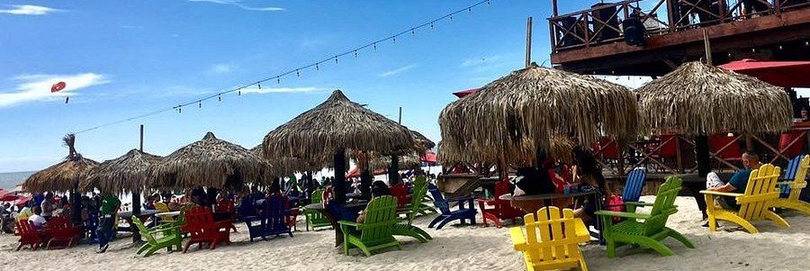 Colorful beachfront seating and palapa umbrellas at Club Iggys in Rosarito Mexico with sandy beaches, ocean views, and a lively coastal atmosphere.