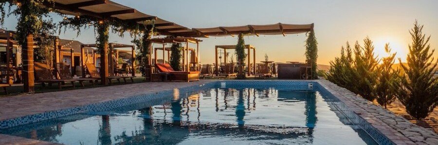 A long rectangular pool at Entrevalle Hotel Boutique in Valle de Guadalupe, reflecting a warm sunset with cabanas and lounge chairs nearby.