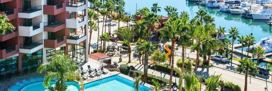 High-angle view of Hotel Coral & Marina in Ensenada, showing the tiered balconies, outdoor swimming pool, and yachts docked in the adjacent marina.