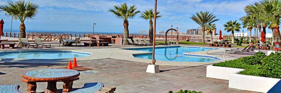 Oceanfront pool area at Las Gaviotas in Rosarito Mexico with palm trees, lounge chairs, tiled patios, and Pacific Ocean coastline views.