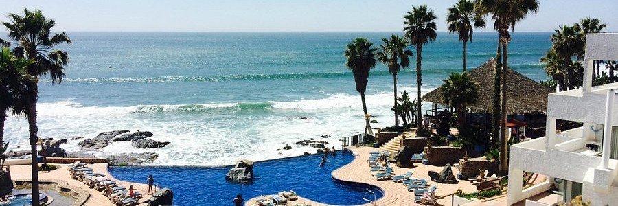 Oceanfront infinity pool at Las Rocas Resort and Spa in Rosarito Mexico with palm trees, rocky coastline, lounge chairs, and Pacific Ocean views.