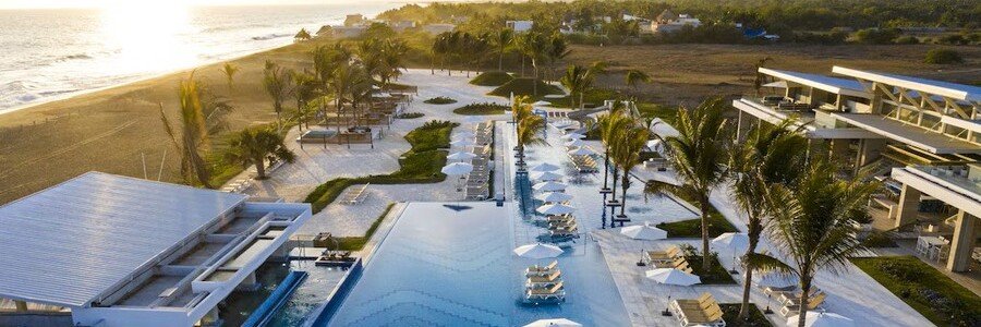 Aerial view of Oceana Delmar Resort in Rosarito Mexico with luxury oceanfront pools, palm trees, beachfront lounge areas, and Pacific Ocean coastline views.