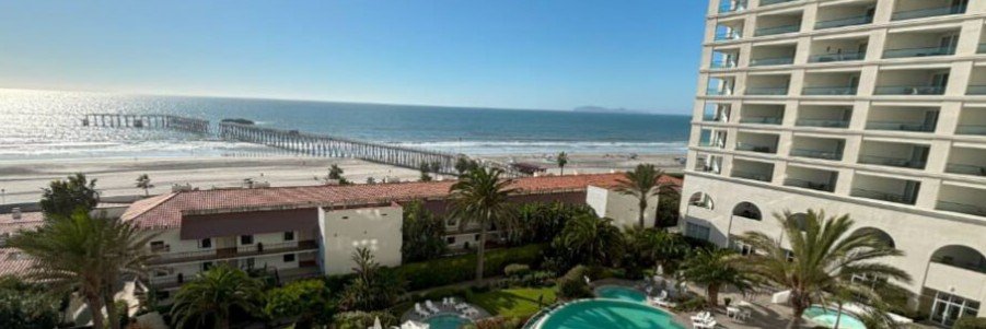 Oceanfront view from Rosarito Beach Hotel in Rosarito Mexico with beachfront resort towers, palm trees, swimming pools, sandy beaches, and a long pier along the Pacific coast.