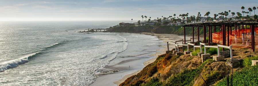 Cliffside coastal view in Rosarito Mexico with rolling ocean waves, sandy beaches, palm trees, and scenic overlooks above the Pacific coastline.