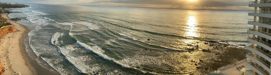 Aerial sunset view of the coastline in Rosarito Mexico with rolling ocean waves, golden reflections on the water, sandy beaches, and oceanfront resort buildings.
