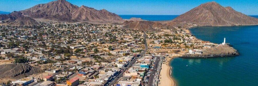 Aerial view of San Felipe, Mexico, showing the white lighthouse on a rocky point, the sandy beach, and rugged desert mountains.