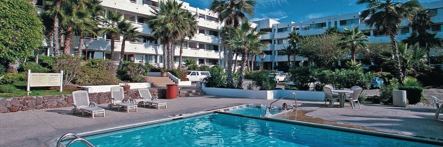 Pool area at Worldmark La Paloma resort in Rosarito Mexico with palm trees, lounge chairs, tropical landscaping, and beachfront condominium buildings.