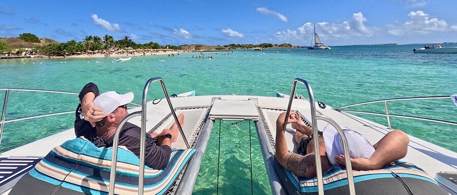 Travelers relaxing on catamaran net over turquoise water near St. Maarten beach with sailboats and tropical coastline