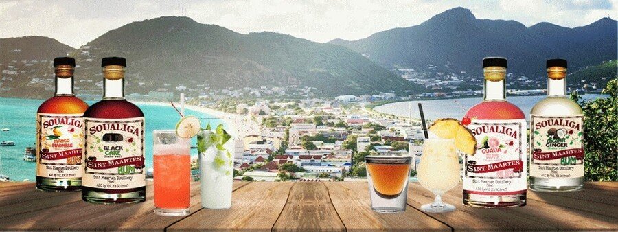 Soualiga rum bottles and tropical cocktails overlooking Philipsburg St. Maarten harbor with mountains and Caribbean coastline