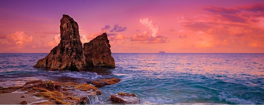 Rock formation at sunset on St. Maarten beach with colorful sky, ocean waves, and Caribbean coastline