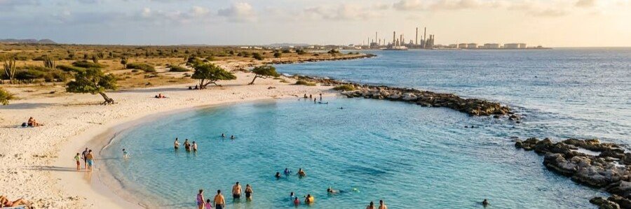 Baby Beach Lagoon Aruba | Beach Travel Destinations Crowd of people swimming in the shallow turquoise water of Baby Beach lagoon with the San Nicolas oil refinery in the background