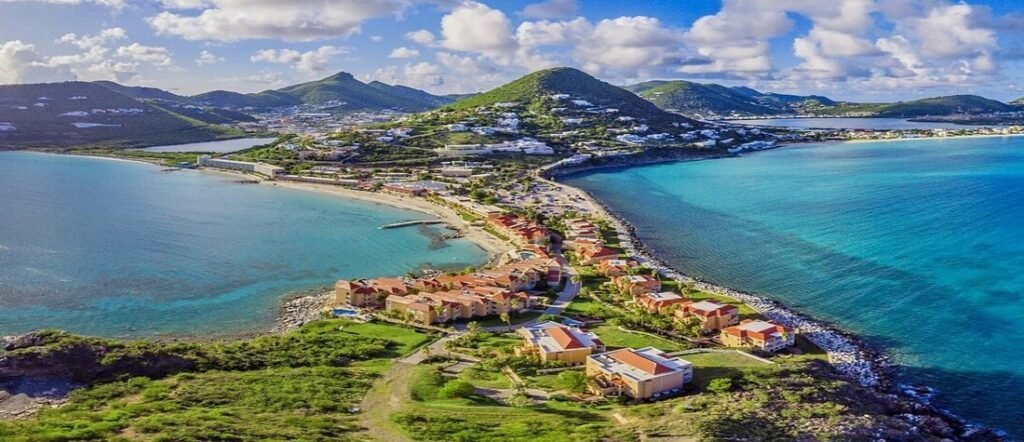 Aerial view of St. Martin coastline showing turquoise Caribbean waters, coastal town, hills, and beaches.