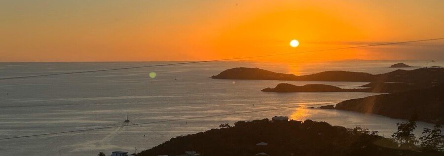 Sunset over St thomas harbor with glowing orange sky, calm ocean, and silhouetted islands