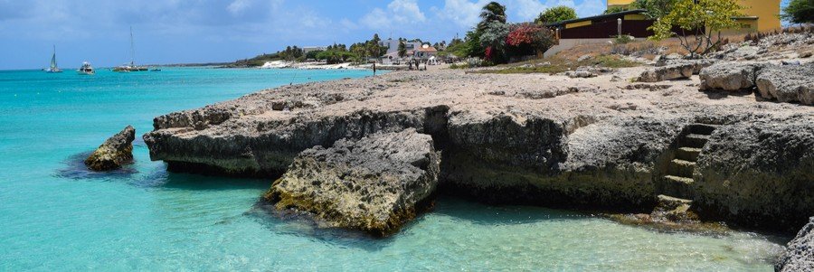 Tres Trapi Steps Aruba | Beach Travel Destinations Stone steps carved into a rocky limestone cliff leading down to clear turquoise water at Tres Trapi in Aruba