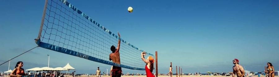 Beach volleyball game with people playing on sandy court by the sea