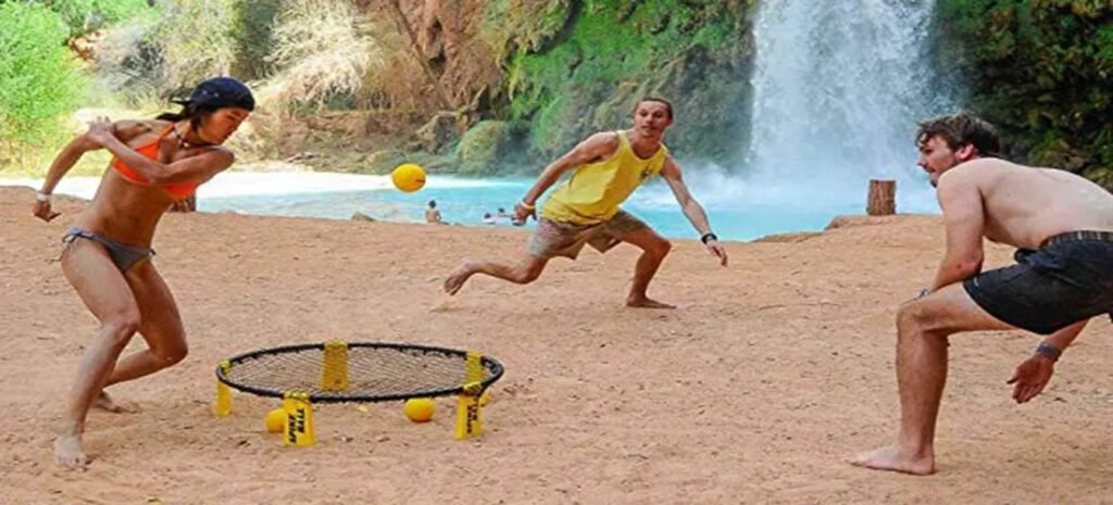 Friends playing Spikeball on the beach near a waterfall, one of the best beach games for active fun.