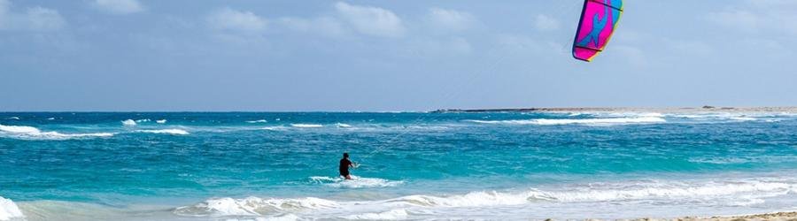 Kitesurfer riding bright blue waves with a colorful kite under a clear sky.
