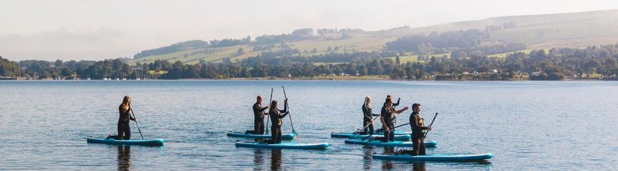 Best stand-up paddleboarding banner – group paddling on calm lake with rolling hills in view
