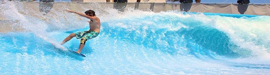 Flowrider surfboard rider performing tricks on a wave simulator with spray in the air.