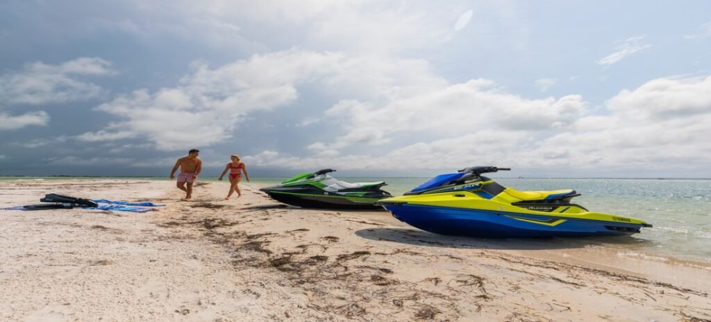 Colorful jet skis lined up on the sandy beach with turquoise waves rolling in at the shoreline. Jet Ski Watersports