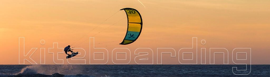 Kitesurfer catching air at sunset with a golden sky in the background.