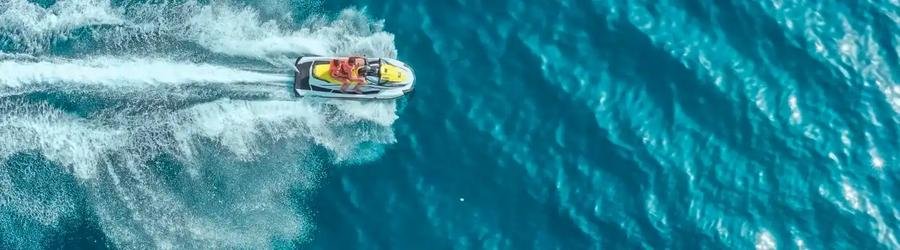Aerial view of a couple riding a jet ski across bright blue ocean waves.