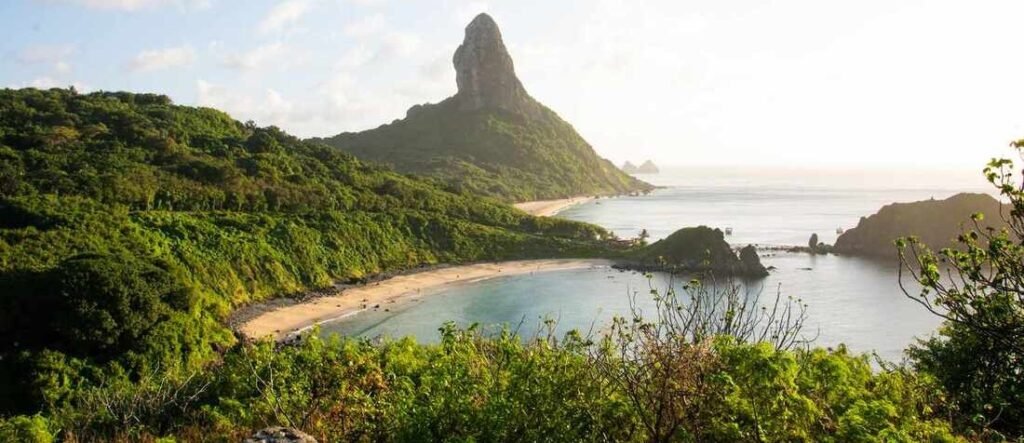 Panoramic high-angle overlook of Baía do Sancho beach in Fernando de Noronha, Brazil, with the signature volcanic peak of Morro do Pico in the background.