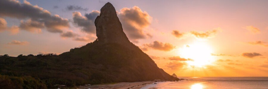 Golden Sunset at Morro do Pico | Beach Travel Destinations Dramatic sunset over the ocean with the towering volcanic peak of Morro do Pico silhouetted against a golden sky in Fernando de Noronha.