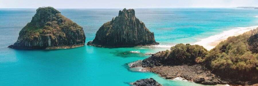 Morro Dois Irmãos and Baía dos Porcos Vista | Beach Travel Destinations High-angle panoramic view of the iconic Morro Dois Irmãos volcanic rock formations rising from turquoise waters at Baía dos Porcos in Fernando de Noronha.