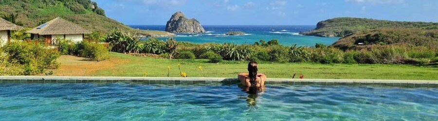 Infinity Pool View at NANNAI Noronha Solar dos Ventos | Beach Travel Destinations Infinity swimming pool and wooden sun deck at NANNAI Noronha Solar dos Ventos hotel overlooking Sueste Bay and rocky islands.