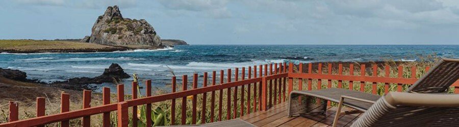 Cliffside Ocean View at Pousada Naonda | Beach Travel Destinations Panoramic view of Pousada Naonda in Fernando de Noronha featuring a brick building with an outdoor wooden viewing deck and private hammock overlooking the ocean.