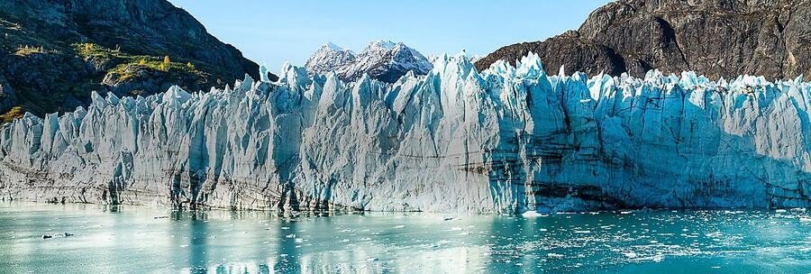 Massive tidewater glacier in Alaska with bright blue ice walls meeting calm water during scenic cruise