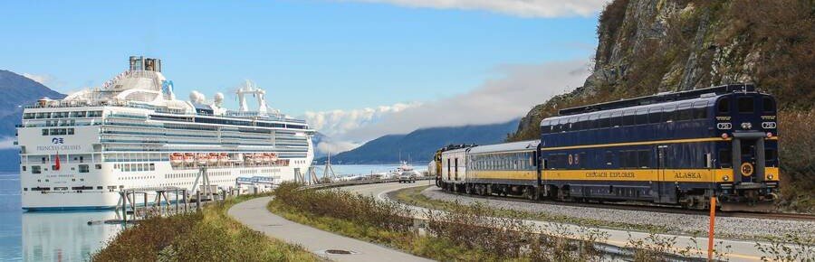 Alaska cruise ship docked near Alaska Railroad train along scenic coastline