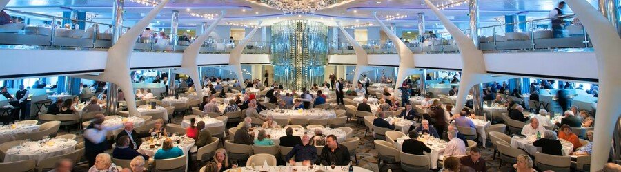 Elegant cruise ship dining room filled with guests enjoying dinner in a modern, multi-level restaurant.