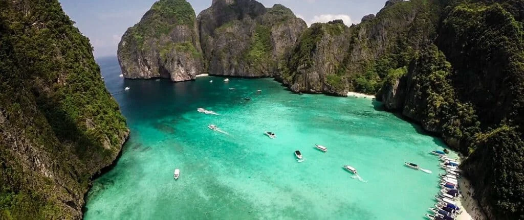 Tropical Phuket Thailand lagoon with turquoise water, limestone cliffs, boats, and sandy beach shoreline
