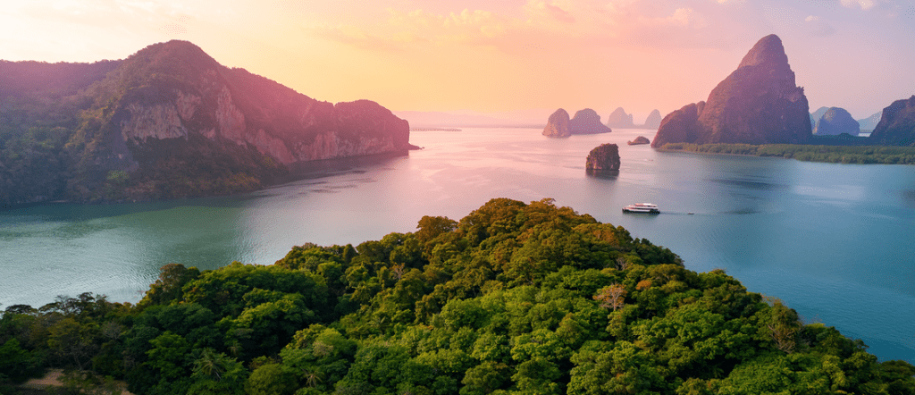 Phuket Thailand island coastline with limestone cliffs, tropical forest, ocean views, and boat at sunset