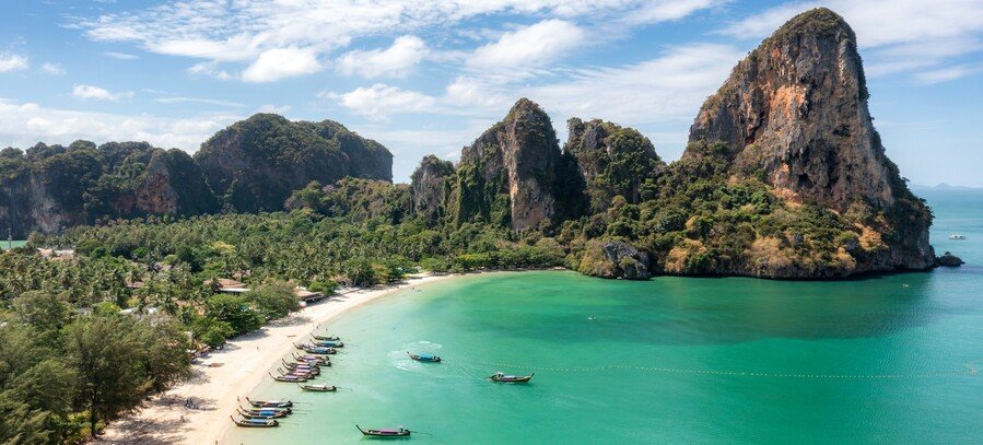 Phuket Thailand tropical bay with limestone cliffs, turquoise water, palm-lined beach, and longtail boats