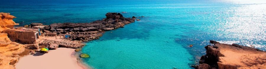 The crystal clear turquoise water cove and rocky shoreline at Calo des Mort beach in Formentera.