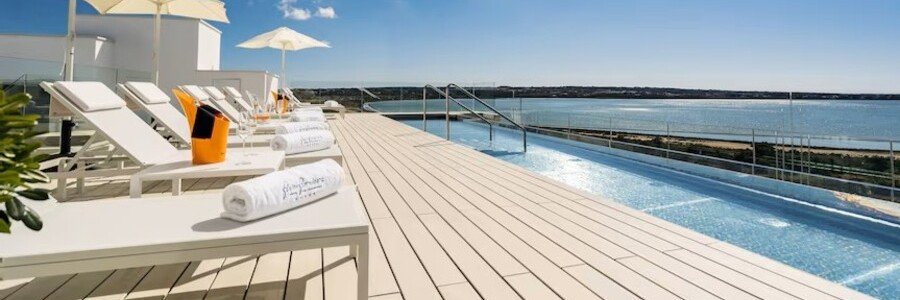 Luxury rooftop infinity pool deck with white lounge chairs and umbrellas at the Five Flowers Hotel in Formentera overlooking the sea.