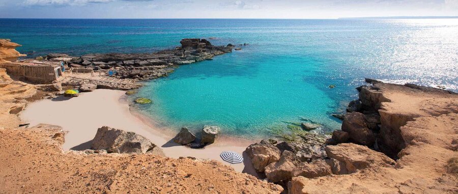 Turquoise cove in Formentera surrounded by rocky cliffs and calm Mediterranean water along the Balearic Islands coastline in Spain.