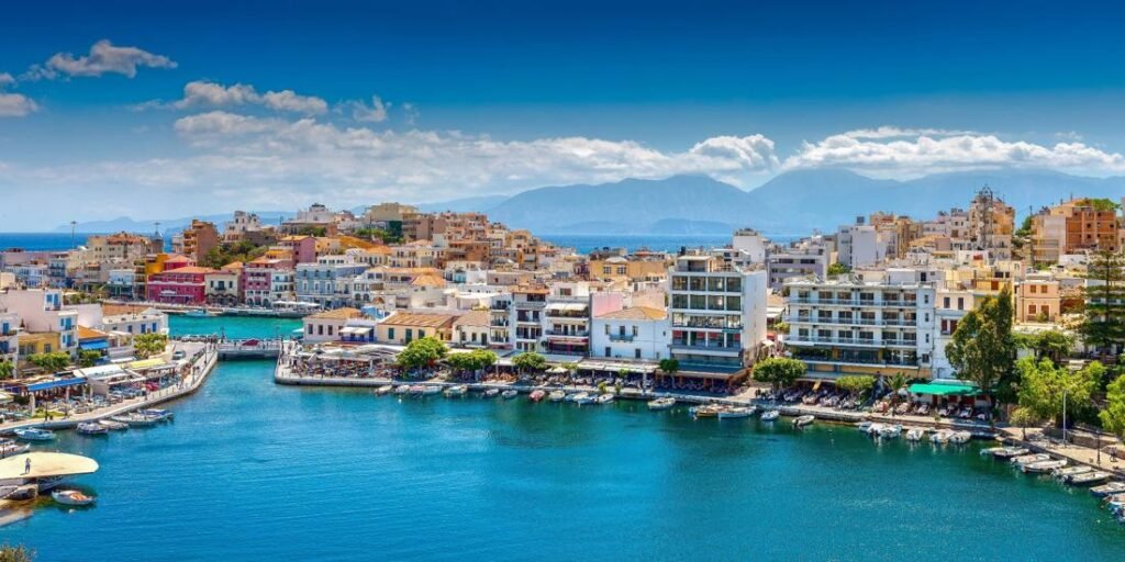 Aerial view of Beautiful Crete Greece with colorful harbor, turquoise waters, and mountain backdrop.