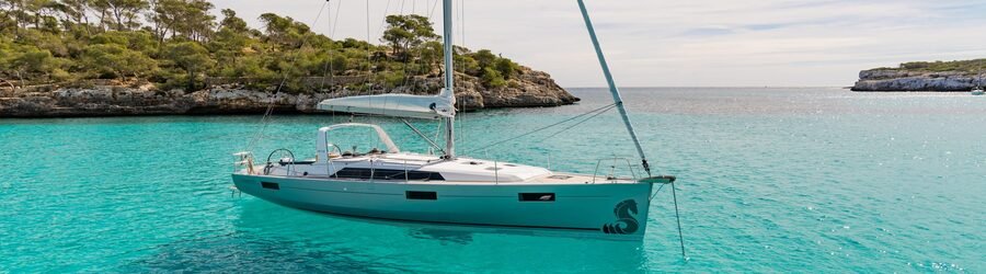 Sailboat anchored in clear turquoise water near rocky coves and pine trees in the Whitsunday Islands.